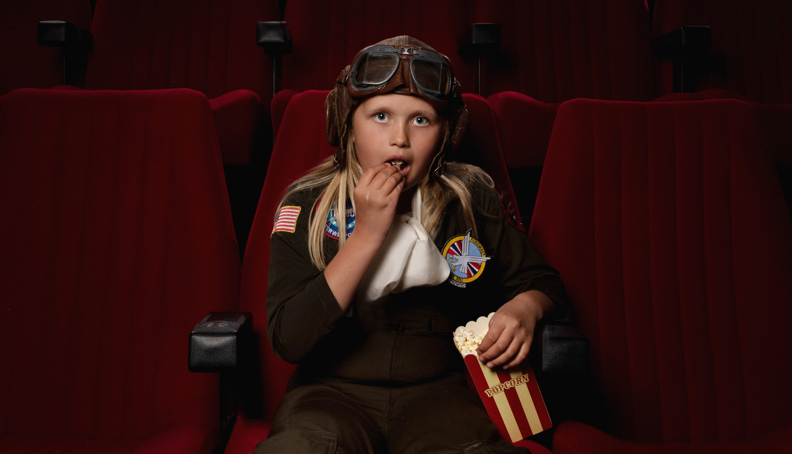 Bilde av jente i pilotdrakt som spiser popcorn i en kinosal